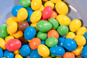Many colorful round candies (hard shell covering a chocolate kernel) inside a bowl, partially cracked and melted. Overhead detail shot.
