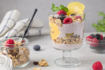 Healthy breakfast. Granola with raspberries, blueberries, golden kiwi and mint sprig. Glass of muesli, berries and yogurt parfait on the table. Vegan natural dessert. Selective focus.