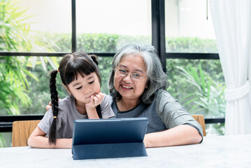 Asian family, Elderly grandmother daughters looking at tablet on marble table in the house, with blur background, to Asian family and children education online concept.