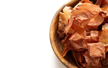 Onions for dyeing eggs. Onion husks in a wooden plate on a white background with copy space. Preparing for Easter.