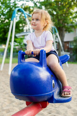 Fototapeta na wymiar Happy child sitting on a carrousel at playground on a sunny summer day. Smiling little girl in park