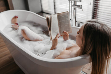 Relaxation and spa day. Carefree woman lying in foamy bath, reading book and enjoying interesting story
