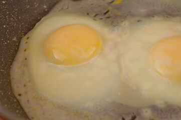 fried eggs in cast iron frying pan sprinkled with ground black pepper on wood table