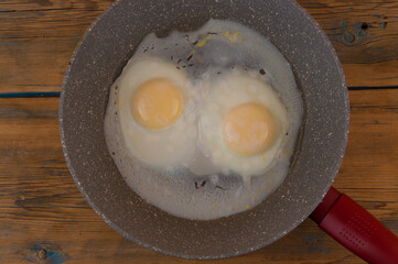 fried eggs in cast iron frying pan sprinkled with ground black pepper on wood table