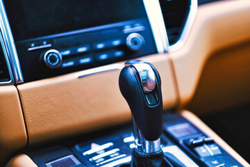 Close up of gear shift handle of a modern luxury sport car with blurred control dashboard panel and leather material texture. Car interior design element.