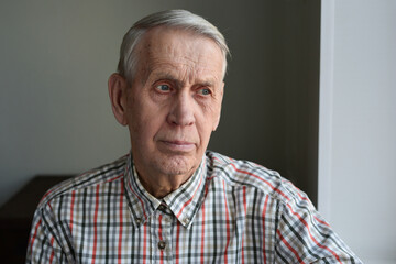Handsome elderly man 80 years old, sad, pensive, looks out the window. 