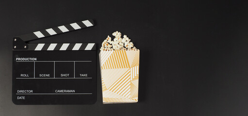 Fototapeta na wymiar Black clapper board or movie slate and a white box of popcorn on black background..
