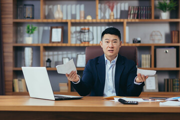 Male Asian businessman refused a loan, frustrated looking at the camera, working in a classic office