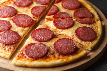 Pepperoni pizza cut on cutting wooden board, selective focus.