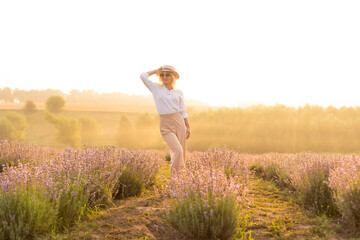 Fototapeta na wymiar Young blond woman traveller wearing straw hat in lavender field surrounded with lavender flowers.