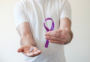 Male hands holding purple ribbon and purple pills.