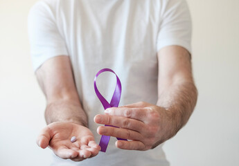 Male hands holding purple ribbon and purple pill.