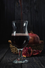 a glass of pomegranate wine or juice against a background of ripe fruit in a basket in a dark key