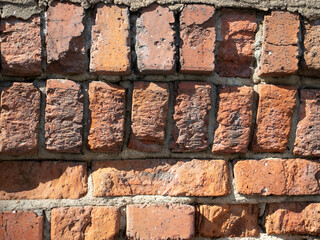 Fragment of old brickwork. Flat lay, close-up. Cracks and defects in the red brick on the wall are illuminated by bright light. Potholes and defects in red brick.