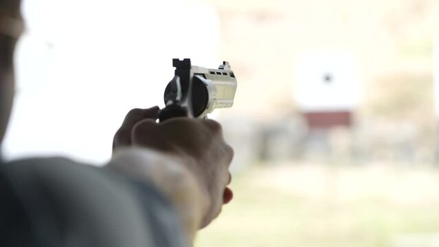 Man shoots with a revolver at targets on the shooting range, close up, blurred focus. Back view of man shooting pistol at target while practicing. Slow motion