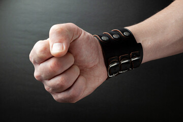 White man's hand in dark leather accessories with a clenched fist stabbing. Punch. Side view, dark...