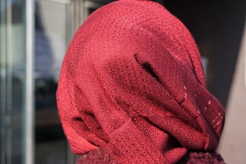 Muslima mit roten Kopftuch mit Muster von hinten auf Straße bei Sonne am Morgen im Frühling