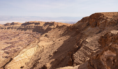 Fototapeta na wymiar section of the south rim of the Makhtesh Katan Small Crater showing cliffs and colorful sandstone with the Jordan Rift Valley in the background