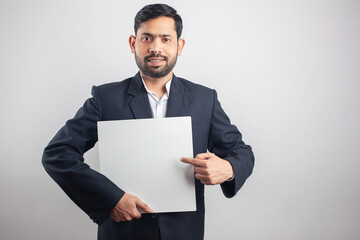 young adult suit man showing and pointing finger towards white empty bulletin board in single color background