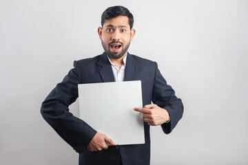 formal dressed indian man pointing finger towards blank placard with surprised expression