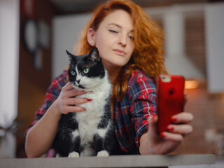 portrait of a beautiful cheerful young woman with a black and white cat in her arms at home. Animals and lifestyle concept. taking selfie on smartphone with pet