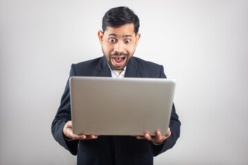 indian man wearing suit looking at laptop screen with surprised expression