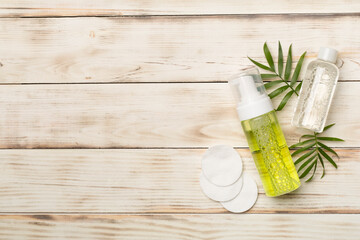 Foaming facial cleanser and micellar water on wooden background, top view