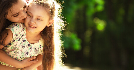 Happy enjoying mother hugging her relaxing laughing kid girl on bright summer green trees background. Closeup family