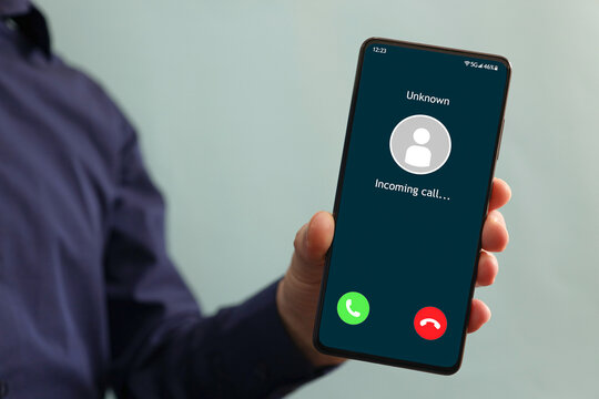 Male Hand Holding A Smartphone With Unknown Caller Displayed On Screen. Unknown Caller Telephony Concept. Incoming Call At Mobile Phone. Prank Caller, Scammer Or Stranger, Privacy, Fraud, Cybercrime.