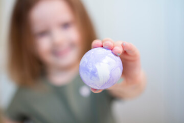 An Easter purple egg in focus in the hands of a little girl. Creative Easter. Selective focus