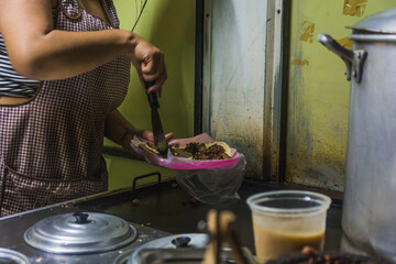 Mexican taquera woman prepares meat and chorizo tacos on the comal at her street stall.