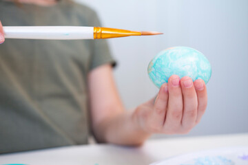 Little girl hand holds brush and paints egg. A process of painting an Easter egg with light green paint. April holiday, close up