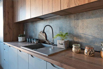 Obraz na płótnie Canvas Modern kitchen interior with kitchen sink with stylish faucet, wooden counter and cabinets and tile pattern on the wall. Cozy home and new apartment.