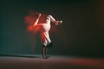 Dancing person moving in freestyle hip hop dance, standing on hands. Long exposure. Contemporary breakdancing school ad