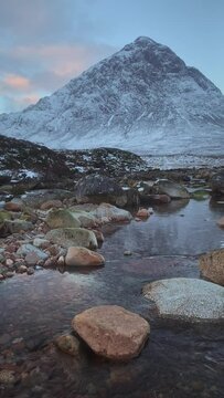 A calm river with stones on the foreground at the foot of a big mountain. Buachaille Etive Mor at the entrance to the valley of Glencoe in the Scottish Highlands, Scotland