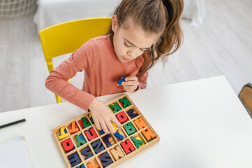 Little schoolgirl playing with wooden letters. Learning to write.