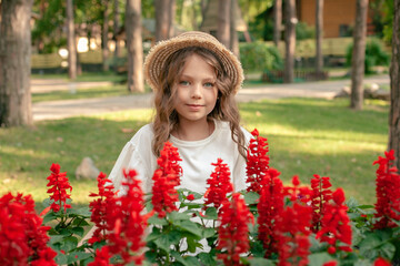Smiling preteen girl posing next to blooming red flowers at country estate