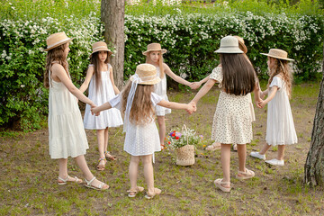 Group of preteen girls in light dresses dancing in circle in green summer park