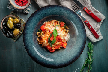 The classic tagliatelli pasta with tomato sauce is served on a blue plate. Italian dish with tomatoes, basil, parmesan and pasta, top view