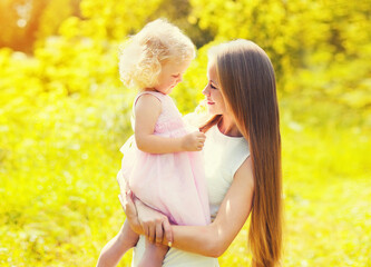 Portrait of young mother holding her little girl baby walking outdoors in summer park