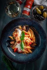 Penne pasta with seafood in a plate on the table. Italian pasta dish with mussels, squid, tomatoes and parmesan, top view