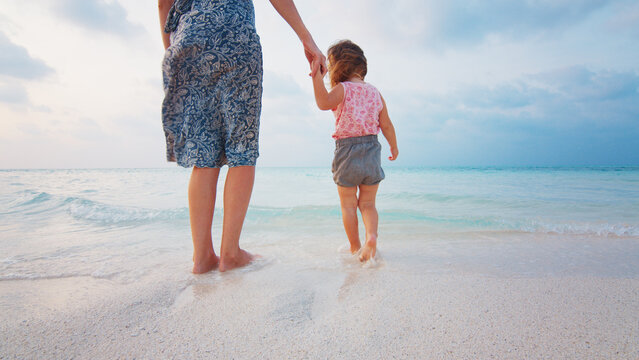 Woman Walks With Toddler Kid On The Tropical Beach During Mellow Sunset In Maldives