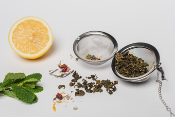 Dry tea in infuser near mint and lemon on white background.