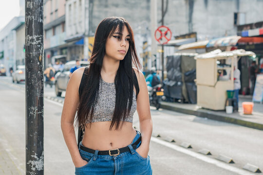 beautiful latina girl with brown skin standing on the street in the city of Pereira-Colombia. university student thinking about her life project with a serious look, while waiting for the bus.