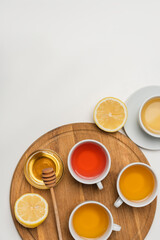 Top view of cups of tea near lemon and honey on chopping board on white background.