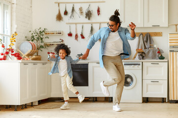 Happy african american family father and little son dancing to music in modern kitchen at home