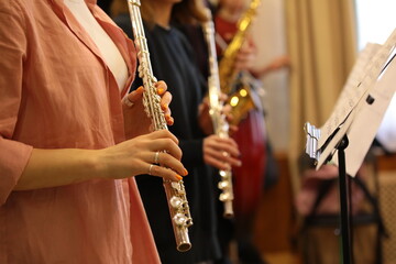 A woman playing a musical instrument flute by notes in a group of musicians practicing in the classroom.A close-up snapshot of the working moment