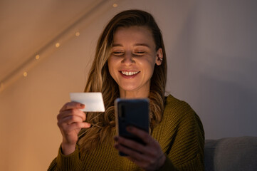 Woman holding credit card and using smartphone while online shopping at home
