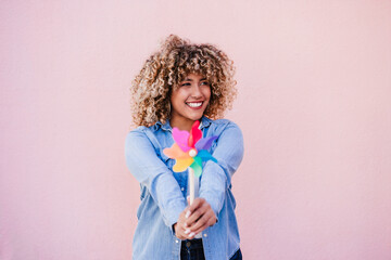 beautiful happy hispanic woman with afro hair holding colorful pinwheel. pink background,wind energy - 494302611