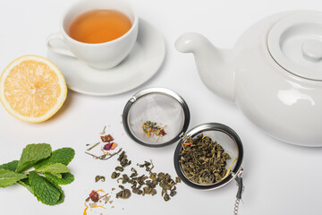 Obraz na płótnie Canvas Dry tea in infuser near mint, lemon and cup on white background.